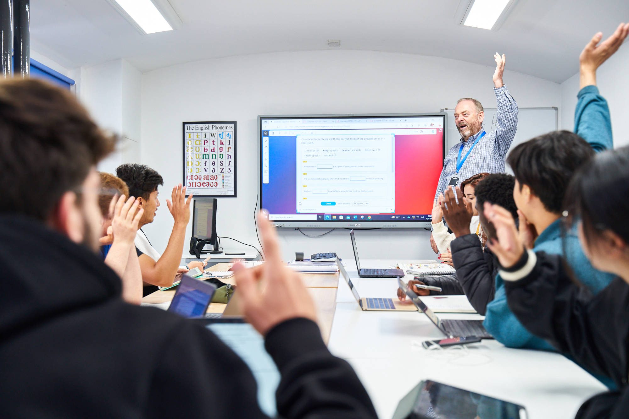 Classroom of pupils with hands up in front of teacher and whiteboard